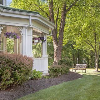 A peaceful garden with a porch and a wooden bench surrounded by lush greenery.