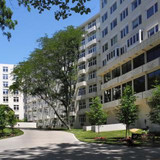 A view of a modern apartment building surrounded by trees under a clear blue sky.