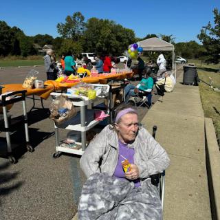 A sunny day at a community event where people gather to participate in food distribution, with a focus on senior citizens enjoying the atmosphere.