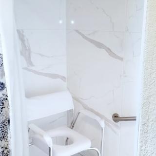 A shower area featuring a white shower chair and marble walls, designed for accessibility.