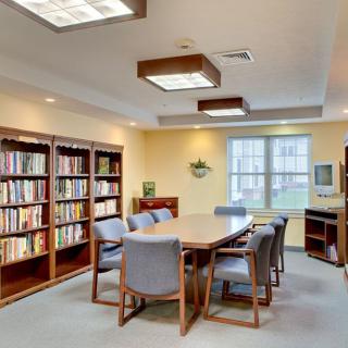 A cozy library meeting room with bookshelves, a table, and chairs by a window.