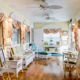 A cozy sunroom with wicker furniture, hardwood floors, and large windows adorned with decorative curtains.