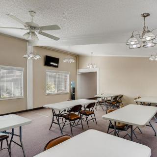 A spacious meeting room with multiple tables and chairs, featuring ceiling fans and chandeliers.