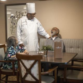 A chef interacting with senior patrons in a dining room setting.
