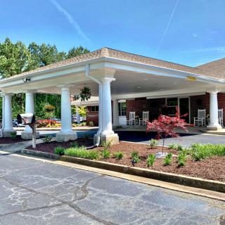 A building entrance with white columns and landscaped gardens under a clear blue sky.