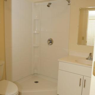 A clean, minimalist bathroom featuring a shower, sink, mirror, and toilet.