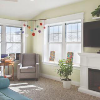 A bright and cozy living room with an armchair by the window, natural light streaming in, a decorative plant, and a fireplace.