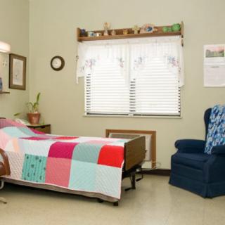 A cozy bedroom with a colorful quilt, armchair, and window with curtains.
