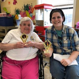 A joyful moment shared between a caregiver and an elderly resident, both proudly holding their trophies.