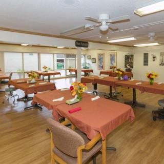 A spacious dining hall with neatly arranged tables and chairs, adorned with flower arrangements.