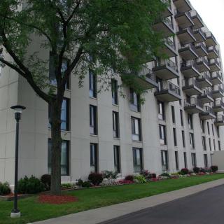 A tall residential apartment building with multiple balconies and landscaping.