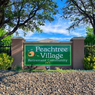 Entrance sign for Peachtree Village Retirement Community surrounded by trees and landscaping.