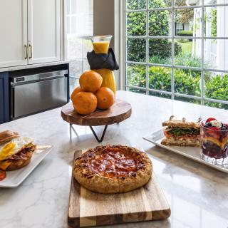 A breakfast spread featuring pizza, sandwiches, fresh oranges, and orange juice on a kitchen countertop.