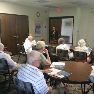 A speaker presents to an audience of elderly attendees in a community meeting.