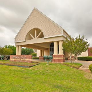 A modern architectural building set against a cloudy sky, surrounded by green grass and trees.