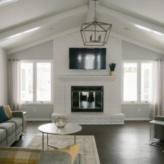 A modern living room with a minimalist design, featuring a central fireplace and overhead TV, flanked by large windows.