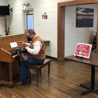 A musician plays the piano in a cozy community center setting.