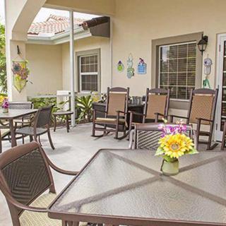 A cozy outdoor patio with multiple tables and chairs, adorned with bright flowers in the sunlight.