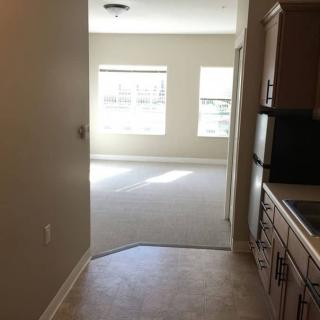 View of a kitchen leading into a sunlit living room with large windows.