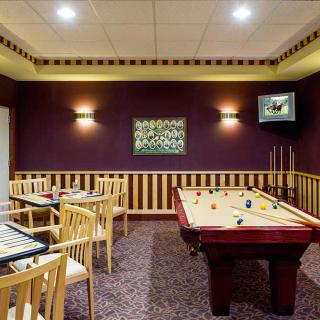 A cozy game room featuring a billiards table and wooden chairs, accented by warm lighting and wall art.