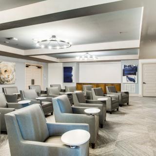 A modern conference room with gray armchairs and round side tables, featuring contemporary artwork on the walls.