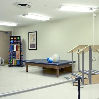 A rehabilitation room equipped with exercise balls, a treatment table, and therapy stairs.