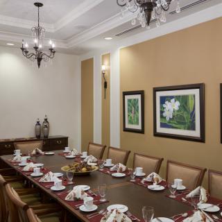A formal dining room with a long table set for a meal, featuring elegant chandeliers and framed artwork on the walls.
