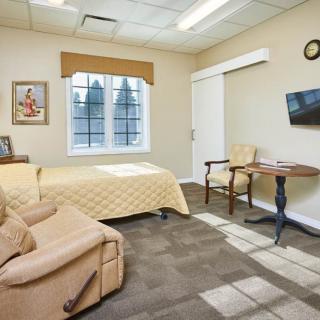 A cozy bedroom with a bed, chair, table, and wall-mounted TV.