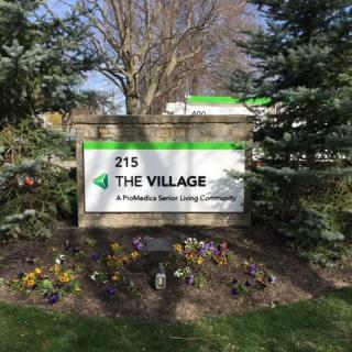 A sign for 'The Village: A Providence Senior Living Community' surrounded by trees and plants.