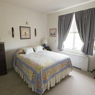 A cozy bedroom with a neatly made bed, wall art, and large windows with curtains.
