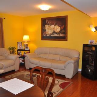 A cozy living room with yellow walls, featuring two sofas, a painting, and warm lighting.
