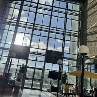 A modern interior space featuring large glass windows that allow natural light to flood in, showcasing a bright sky outside.