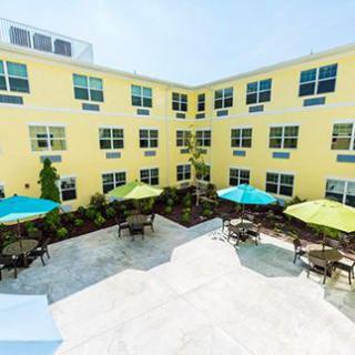 A bright yellow building encloses a courtyard with colorful umbrellas and outdoor seating.