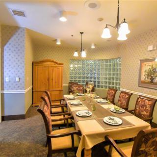 An elegant dining room with a long table set for a meal, surrounded by comfortable chairs and warm lighting.