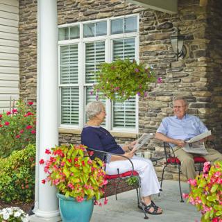 Two seniors enjoying a conversation on a porch surrounded by flowers.