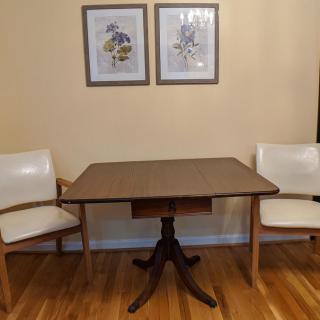 A cozy dining area featuring a wooden dining table with two white chairs and framed artwork on the wall.