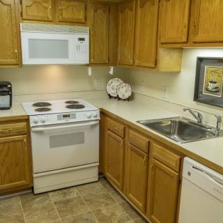 A cozy kitchen with wooden cabinets, featuring a stove, microwave, sink, and dishwasher.