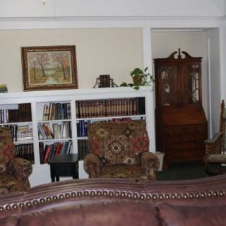 A cozy living room featuring bookshelves, floral armchairs, and a decorative cabinet.