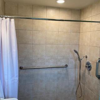 A bathroom shower area with beige tiles, a shower curtain, and a wall-mounted showerhead.