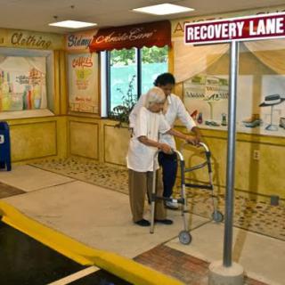 An elderly person receives assistance while using a walker in a recovery-themed setting.