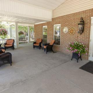 A cozy porch with wicker furniture and decorative plants against a brick wall.