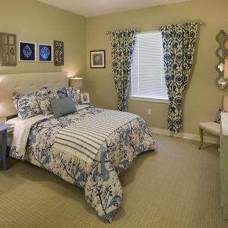 A cozy bedroom with patterned bedding and curtains, adorned with artwork and warm lighting.
