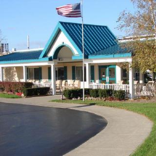 A small building with a blue roof and an American flag displayed outside, surrounded by a driveway and trees.