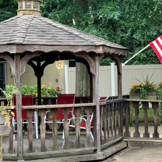A charming wooden gazebo with red chairs, surrounded by lush greenery and adorned with an American flag.