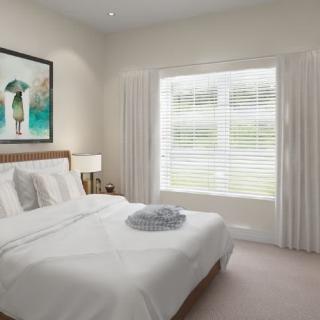 A minimalist bedroom with a neatly made bed, artwork on the wall, and natural light filtering through a window with blinds.