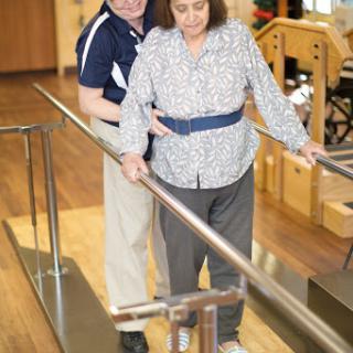 A physical therapist assists an elderly patient during rehabilitation, helping them navigate a ramp.