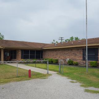 An exterior view of a brick building, possibly a school, surrounded by grass and pathways.