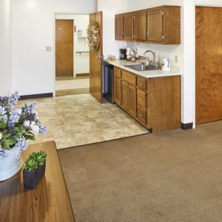 A clean apartment kitchen with wooden cabinets and a sink, featuring a small dining area adorned with potted flowers.