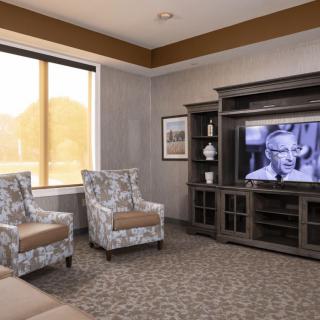 A cozy living room with patterned chairs and a television playing a black-and-white film.