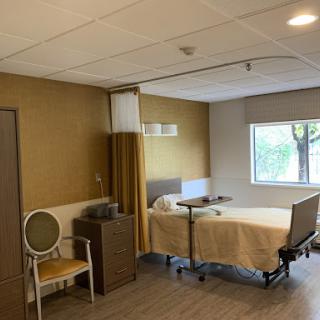 A view of a hospital patient room featuring a bed, chair, and window.